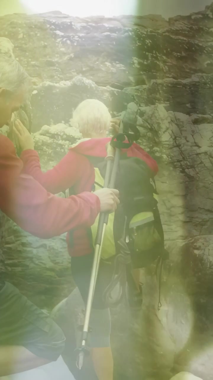 Vertical video: Lead hiker reaching handrail and climbing trail to ascend, companion holding poles