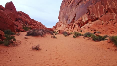 Rainbow-Vista-Trail-Walking-Over-Red-Sand-with-Surrounding-Rocks,-POV,-Nevada,-USA