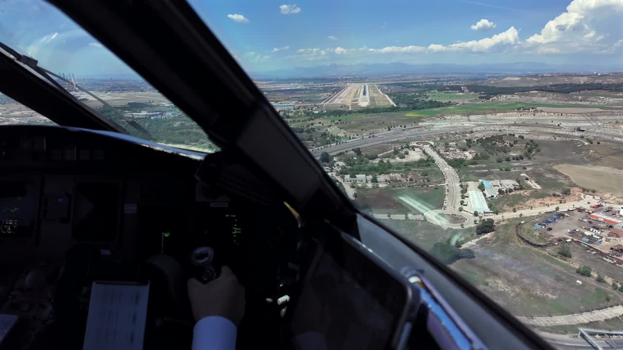 Pemandangan imersif dari sudut pandang pilot melalui jendela pesawat jet yang menerbangkan kontrol penerbangan secara manual dengan landasan pacu di depan, dengan langit biru berawan tipis