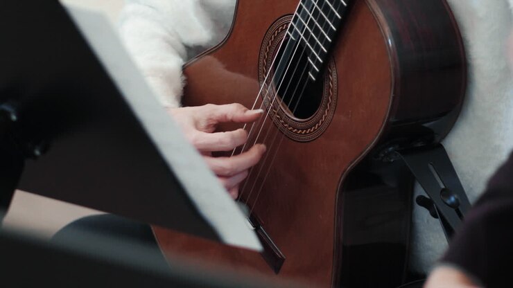 Dettaglio di una chitarra classica e mani femminili che la suonano.