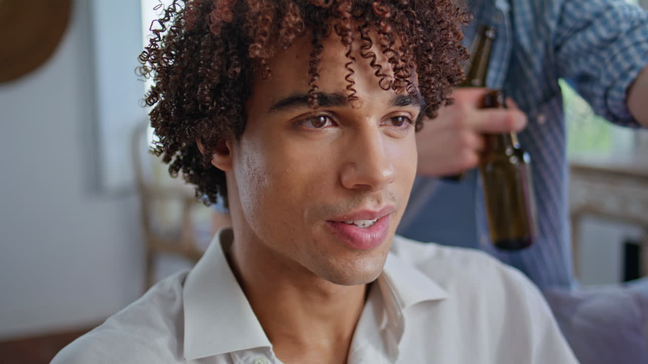 Curly guy watching tv at party with classmates closeup. teen hanging out