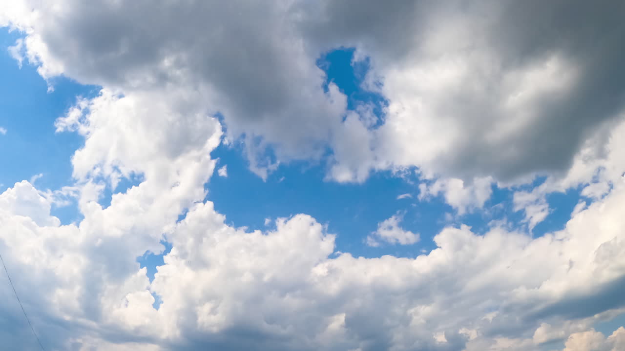 Soft light white clouds quickly floating by the azure skies. Soft clouds gathering into a big cloudscape. Low angle view timelapse.