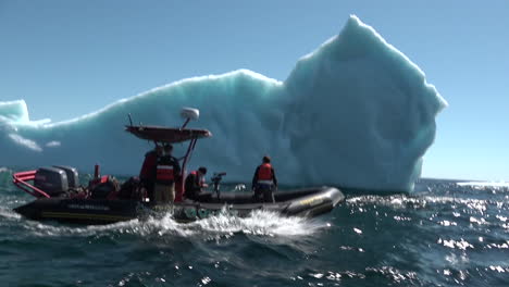 researchers in a zodiac boat pass a massive iceberg in the arctic