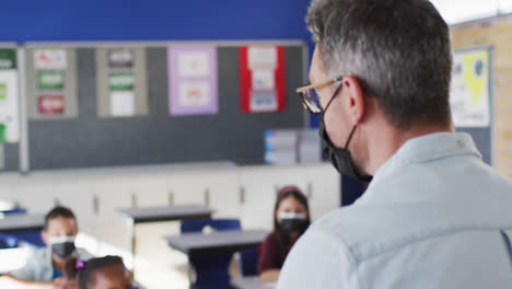 diverse teacher conducting lesson in classroom with children, all wearing face masks