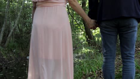 Slow-Motion-Back-view-of-couple-walking-hand-in-hand-in-woods-near-stream-banks