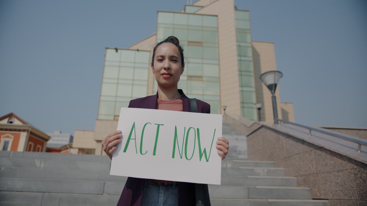 Woman holding a sign that says ACT NOW on the city stairs