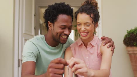 Happy-biracial-couple-embracing-with-joy-and-holding-keys-in-front-of-new-house