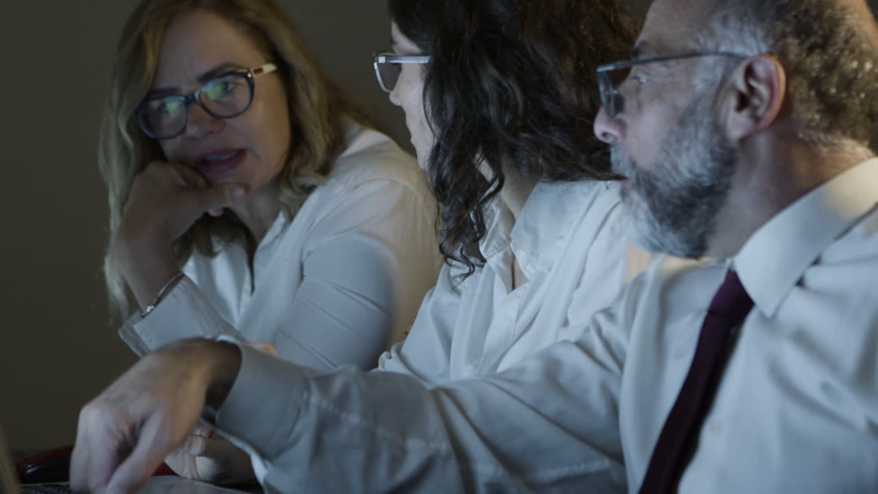 동료 들 이 어두운 사무실 에서 프로젝트 를 논의 하고 있다