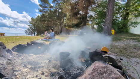 view of a girl drinking water beside an extinguished bonfire during daytime.