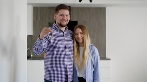 cheerful young man and woman standing in the apartment and showing the keys