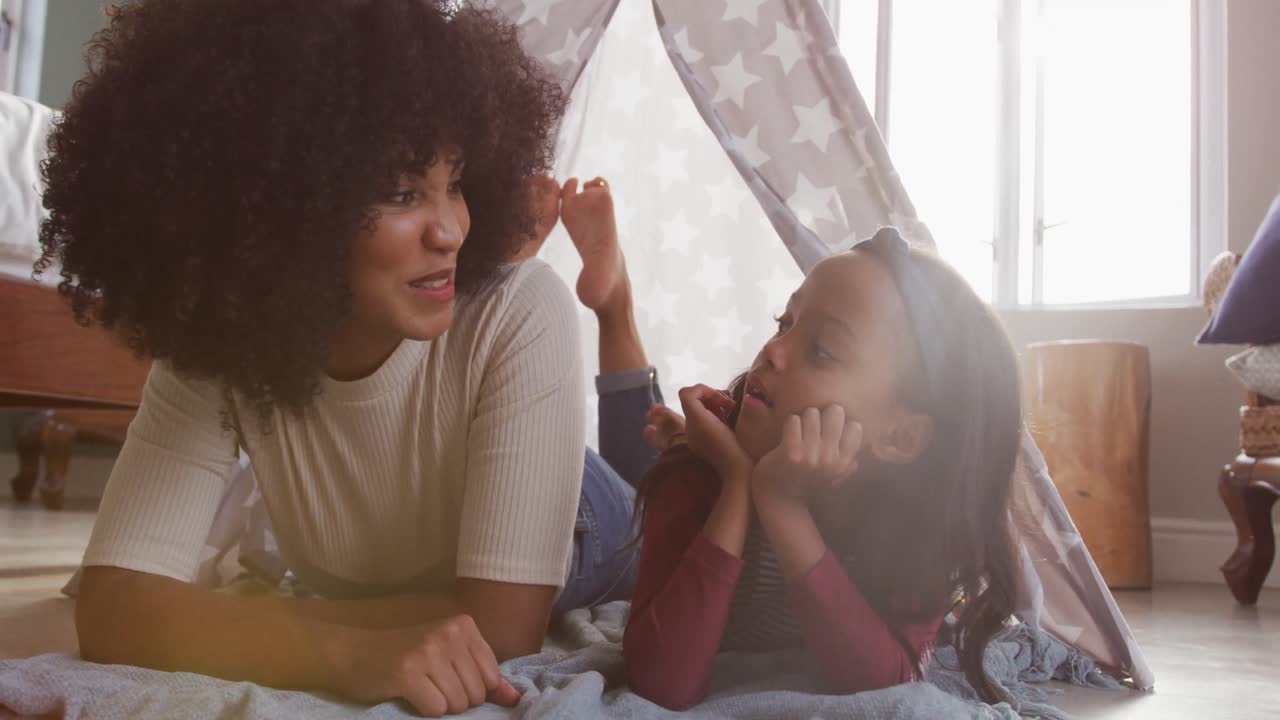 video de una feliz madre y hija afroamericanas acostadas en una tienda de campaña y hablando juntas
