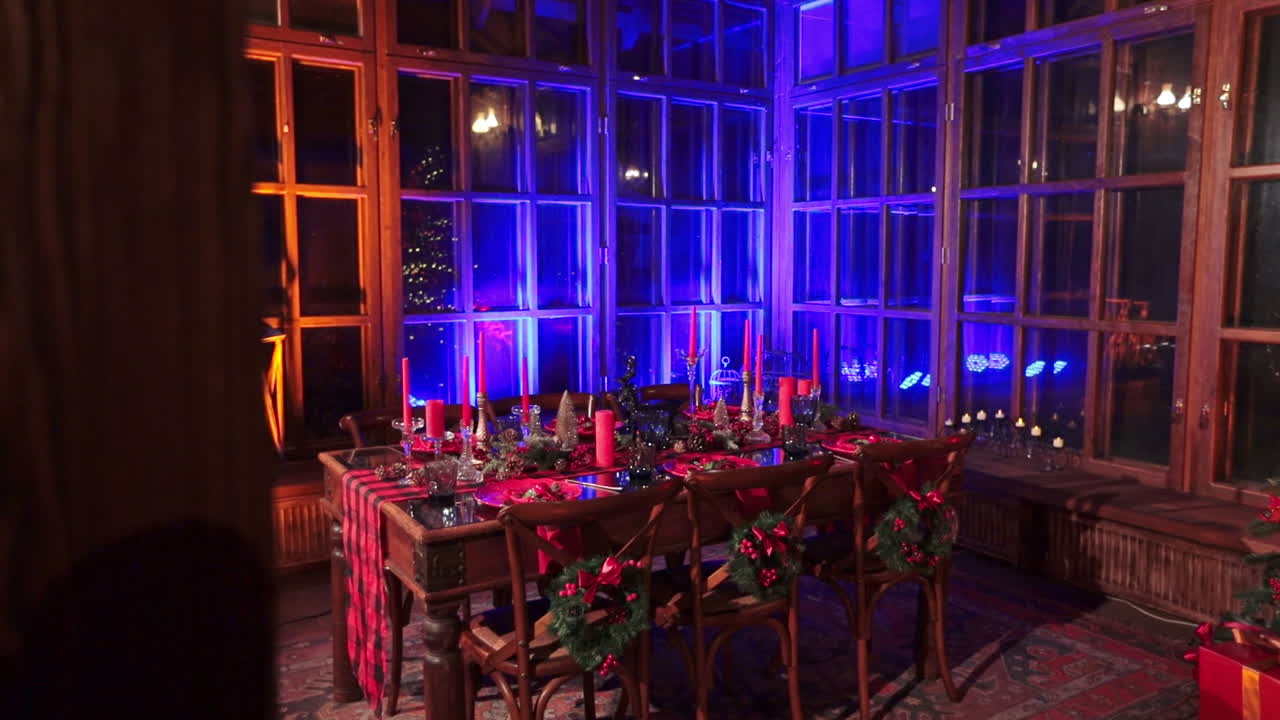 Laid table with lots of Christmas decors and festive crockery for six persons. Big window wall of a country house at backdrop.
