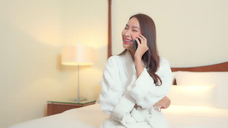 happy asian woman in bathrobe on smartphone having night call chat in a bedroom