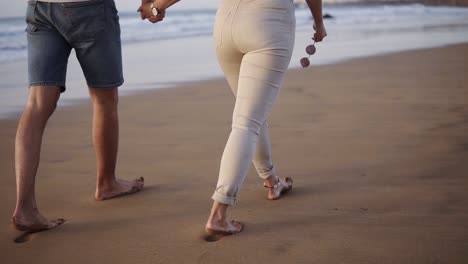 married young couple on beach walking in love holding hands at romantic sunrise. woman and man relaxing on travel vacation holidays, wearing casual clothes. slow motion. rare view