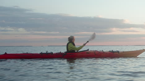 young blonde woman paddling in a red sea kayak on the open sea in finland, vaasa, archipelago, beautiful summer sunset atmosphere, dawn, close-up