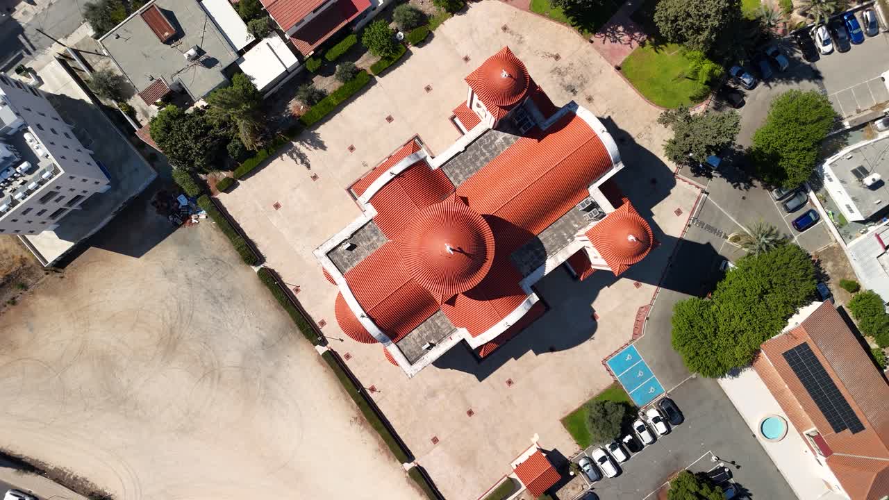 A beautiful church with a striking red dome stands out in a peaceful area filled with houses and green trees. The layout shows parking spaces and nearby structures