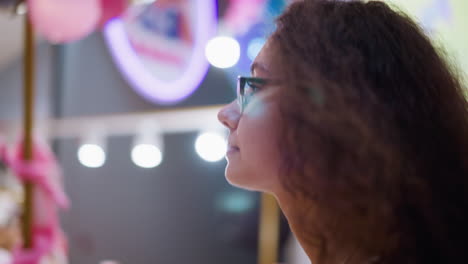 lady with curly hair and glasses walking through well-lit mall, displaying a calm and focused expression, blurred background reveals bustling retail environment with stores and people