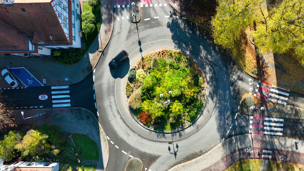 Top-down drone shot of green roundabout surrounded by city streets, cars, and crosswalks in Sopot, Poland
