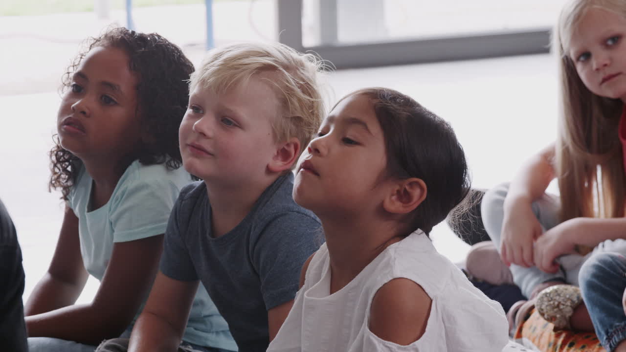 교사 의 말 을 듣고 바닥 에 앉아 있는 초등학교 학생 들 의 그룹