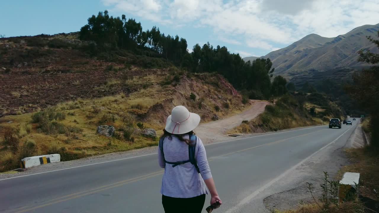 Woman with traditional peruvian hat walks along rural mountain road with cars passing by.. Puka Pukara archaeological ruins surroundings