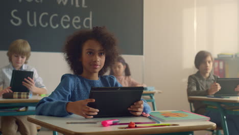 Niña-Afroamericana-Sonriente-Usando-Tableta-Digital-En-Clase-Con-Compañeros-De-Clase