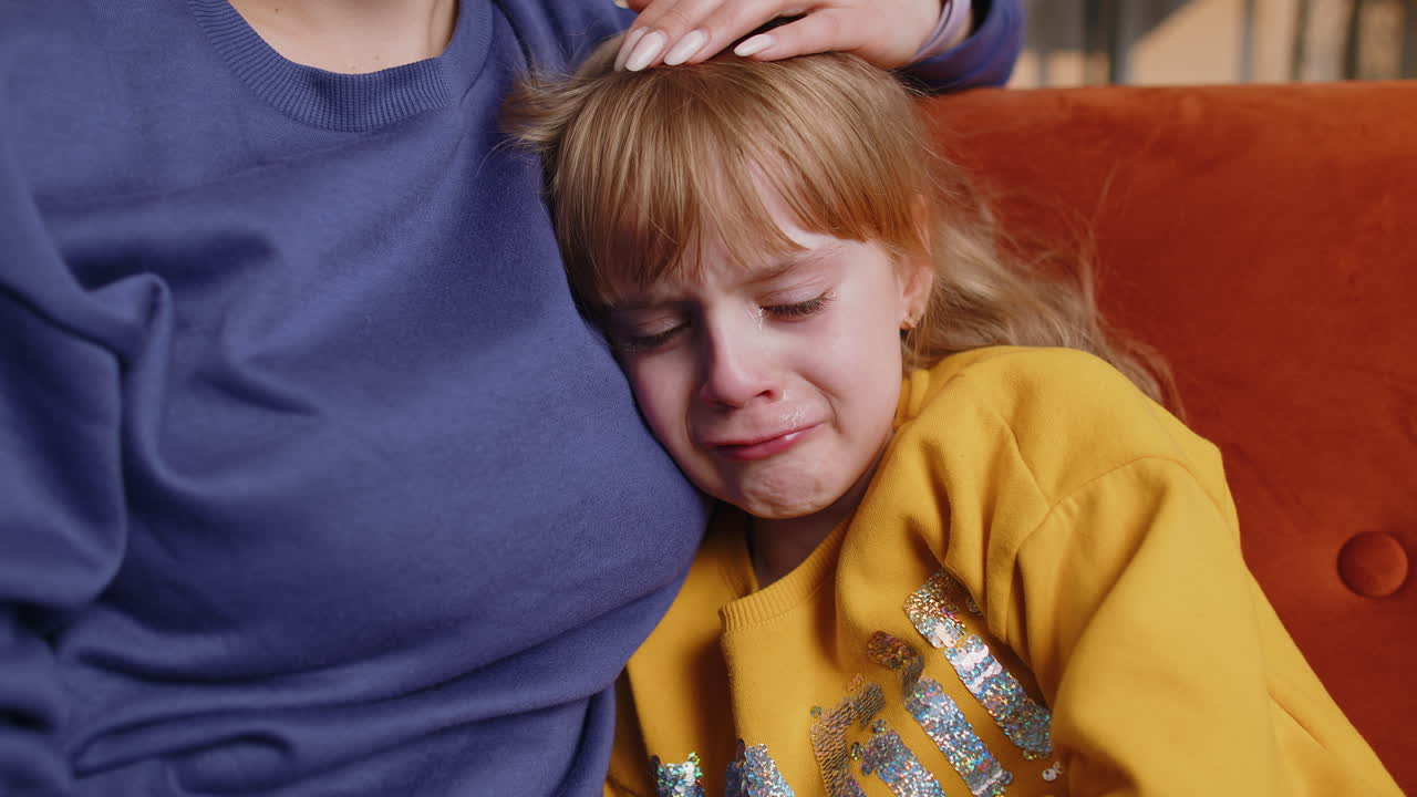 Upset child little girl kid crying with tears flowing down on cheek toddler lies on mother at home