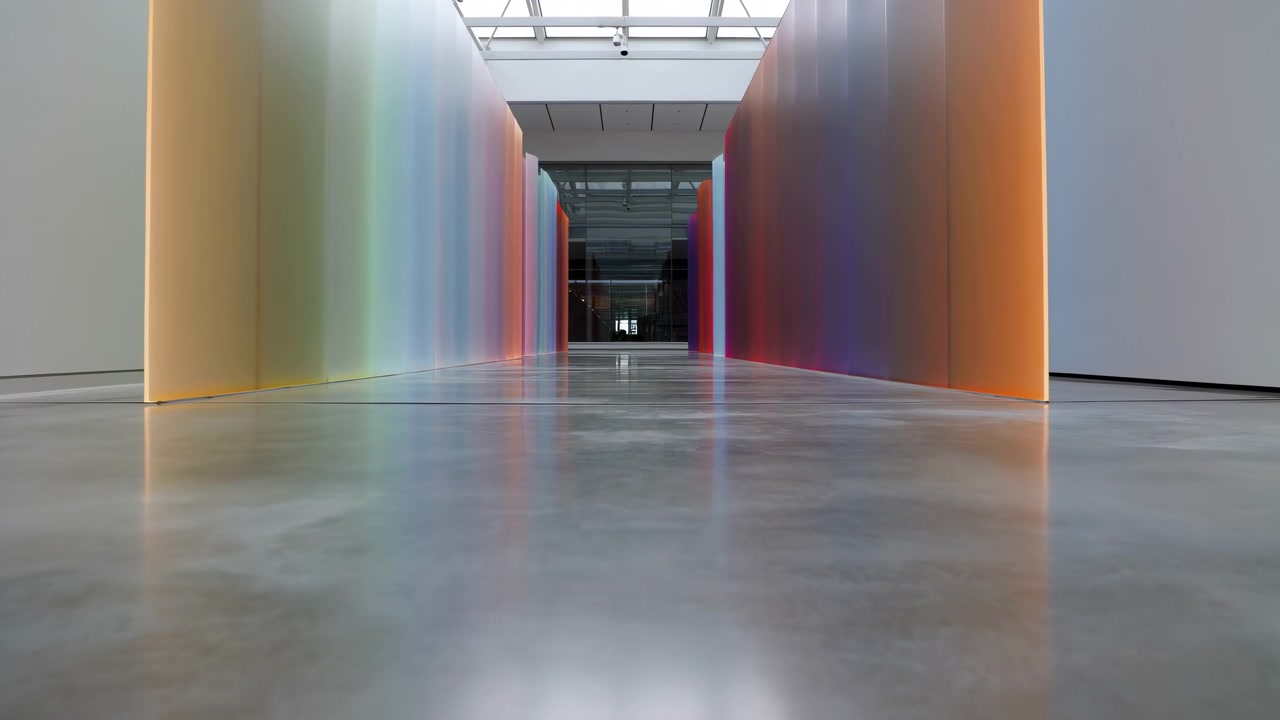 Vista baja y centrada de un elegante pasillo interior con altos paneles translúcidos de colores a ambos lados, reflejos de un suelo de hormigón pulido y luz diurna suave