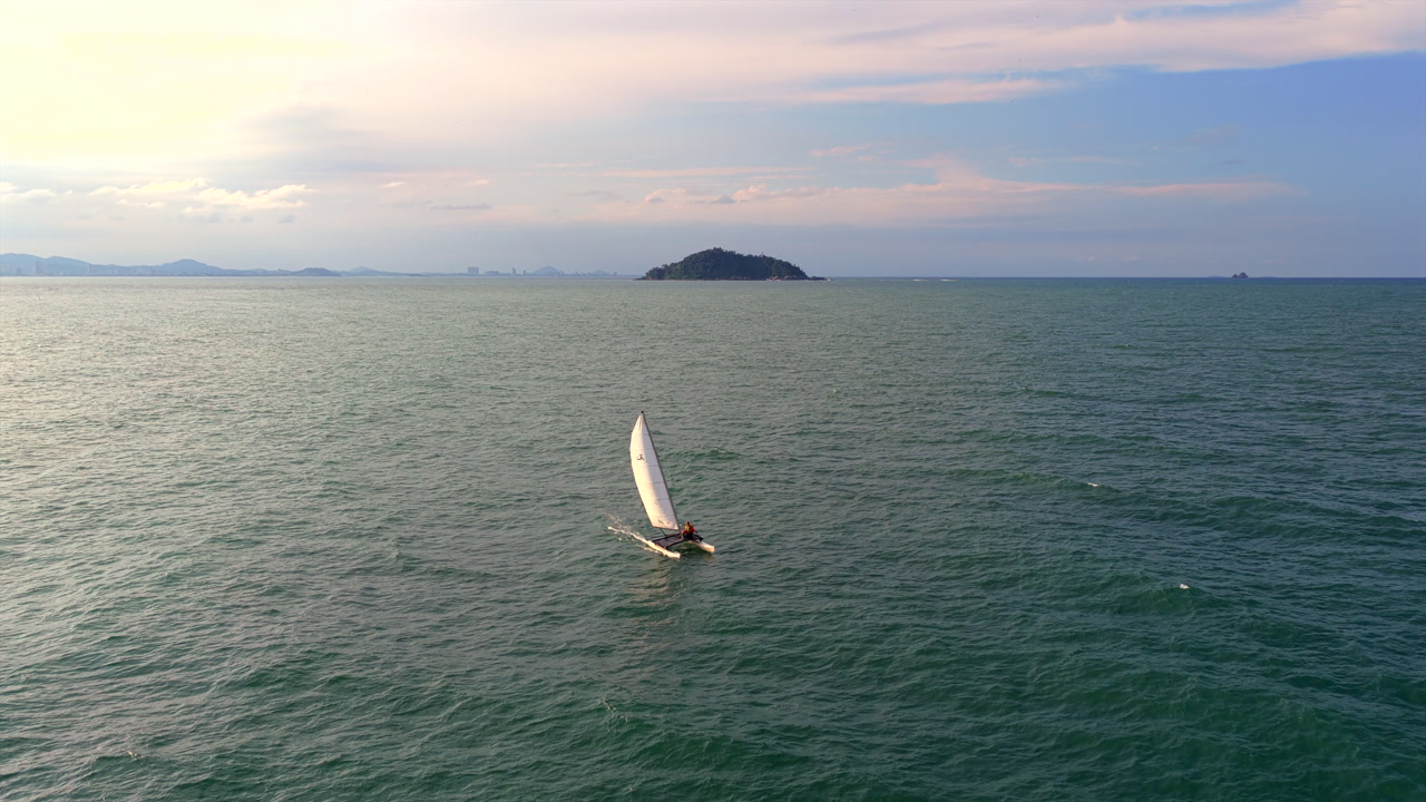 Aerial drone view of a sailboat navigating the open sea near Ilha Feia island in Santa Catarina, Brazil.