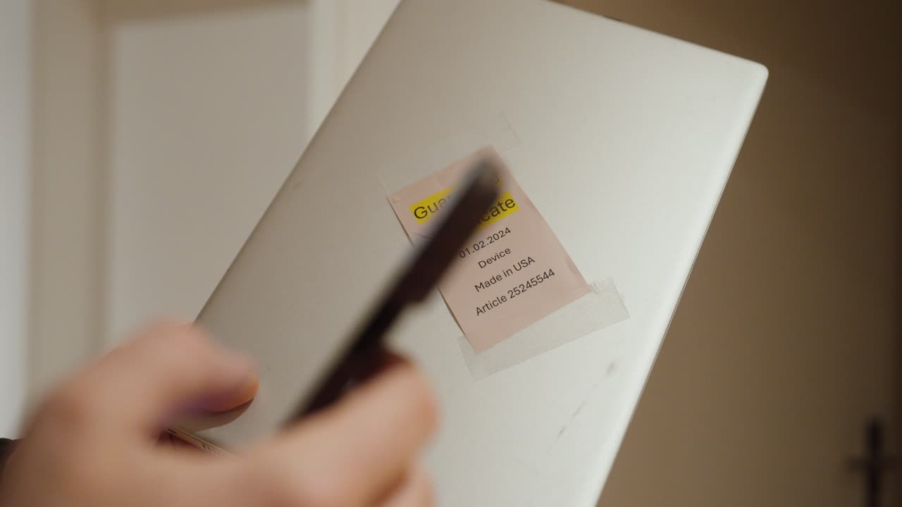 a person holding a device with a guarantee certificate label and using a smartphone to request warranty repair. Concept of consumer rights, product warranty, customer service and repair process