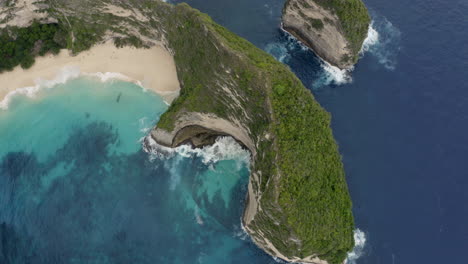 top view of steep cliffs at kelingking beach with waves crushing ashore, nusa penida, bali, indonesia. aerial shot