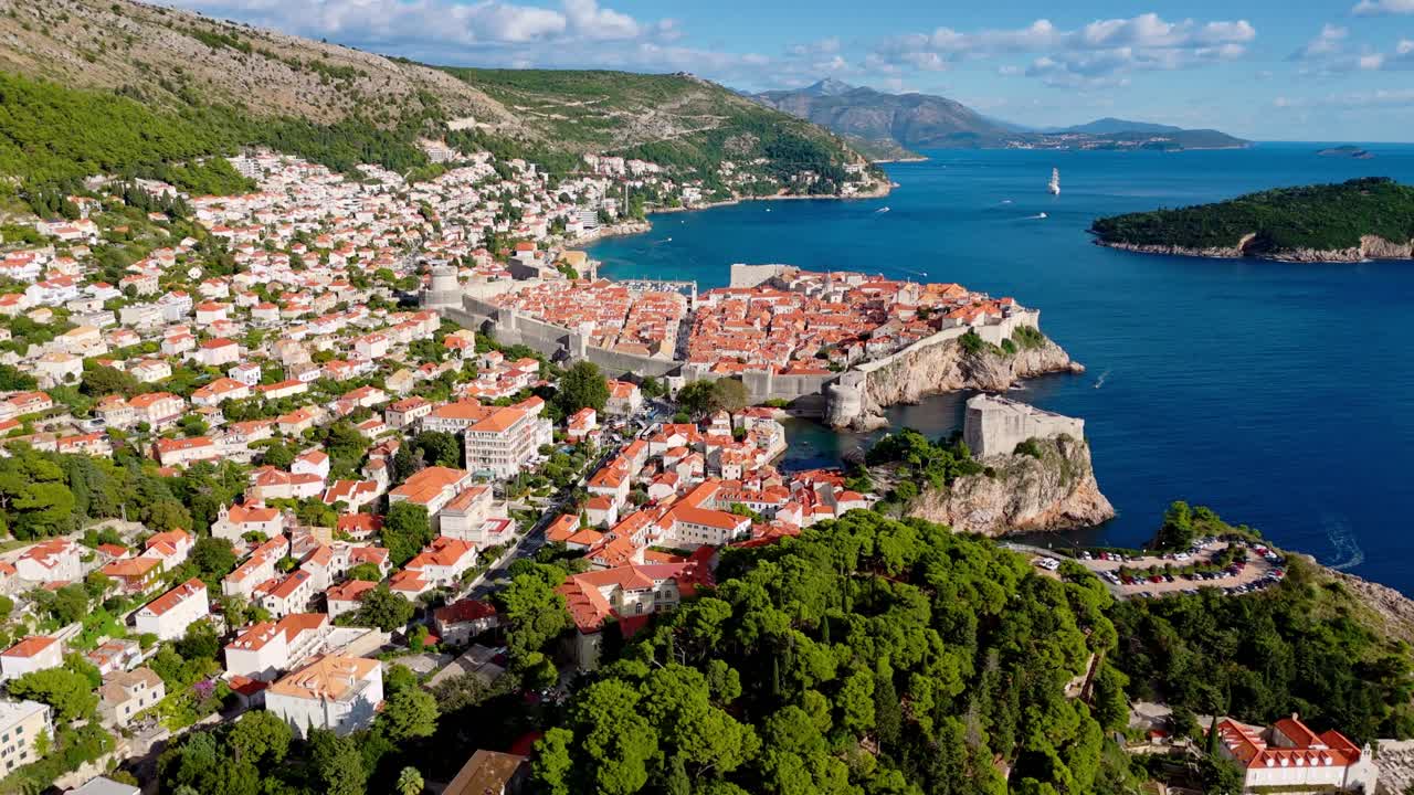 Wide-angle aerial drone pans over Dubrovnik’s Old Town, revealing terracotta rooftops, winding streets, the deep blue Adriatic Sea, and rugged mountains in the background, all illuminated by sunlight