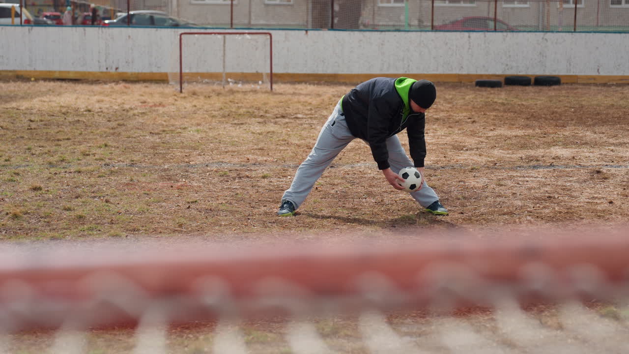 player lunges to catch ball, sportsman leans in to seize ball, fencer stretches out to grab ball before goal, athletic individual moves forward to reach for ball quickly during play