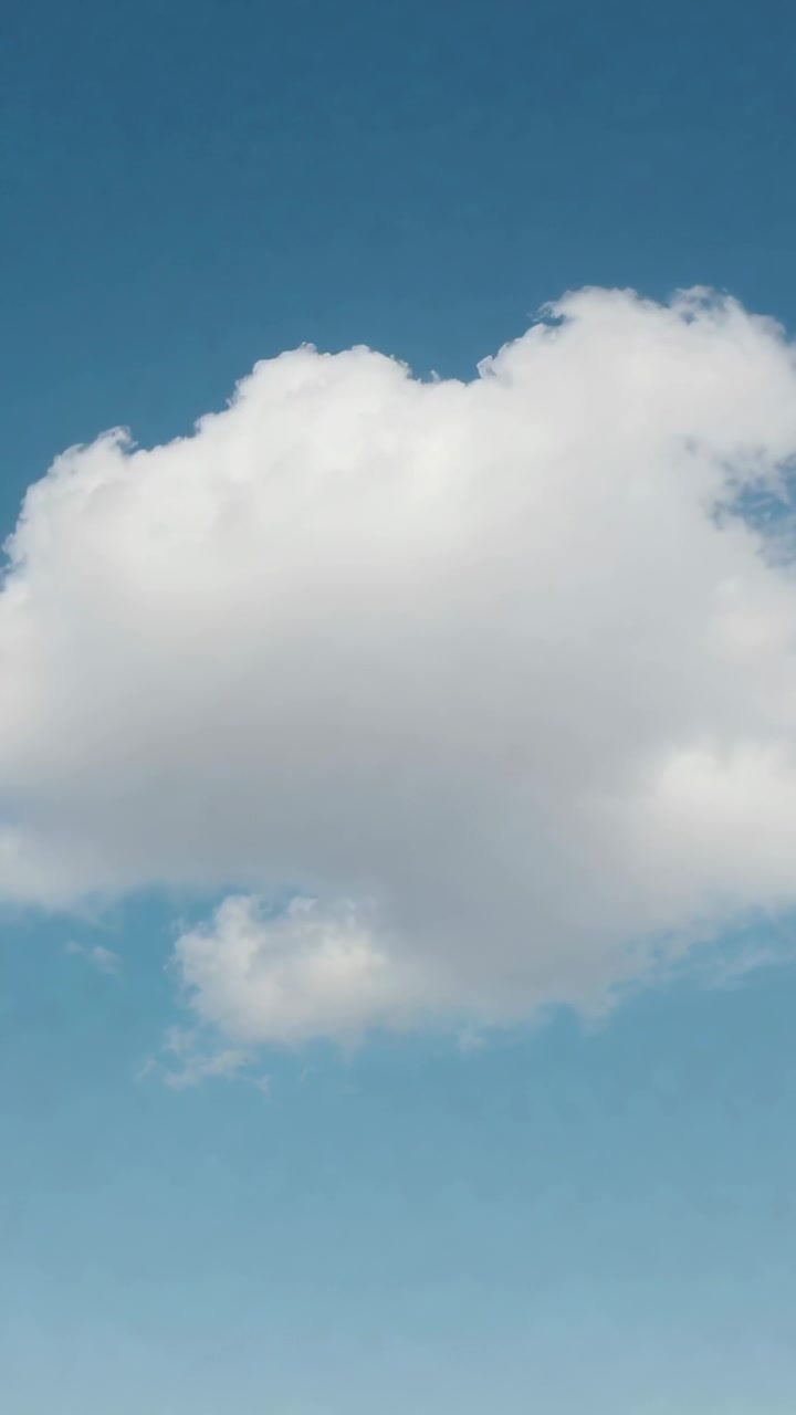 Video vertikal: Awan kumulus besar tunggal melayang, berubah bentuk di langit biru cerah, didorong angin sepoi-sepoi