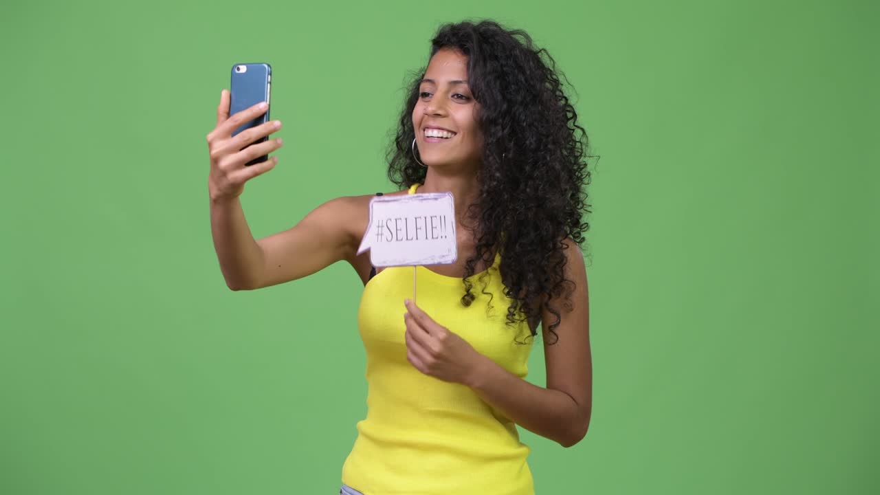 Young beautiful Hispanic woman taking selfie with paper sign