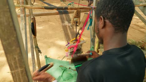 joven hombre africano tejiendo seda tradicional kente y algodón en telares