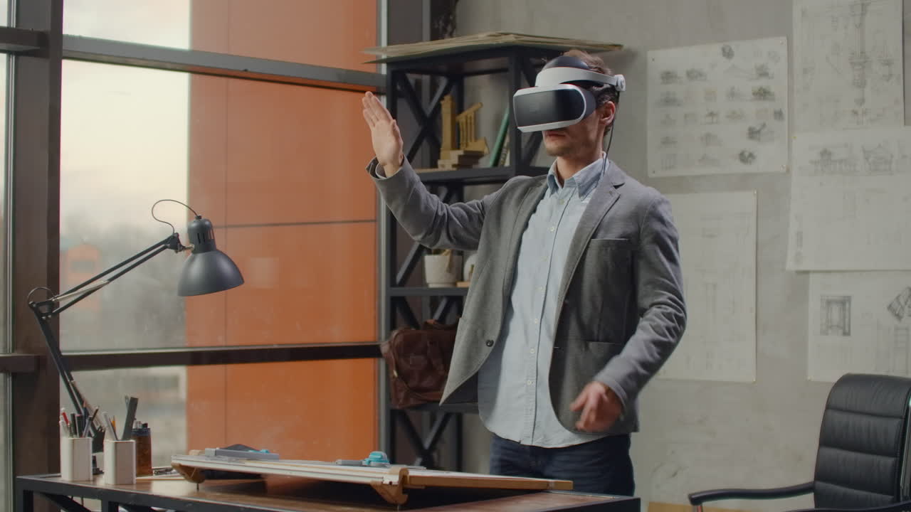 Modern man architect in the office with large windows stands in a virtual reality helmet uses gestures to manage the project without leaving the office. Construction control. Design project