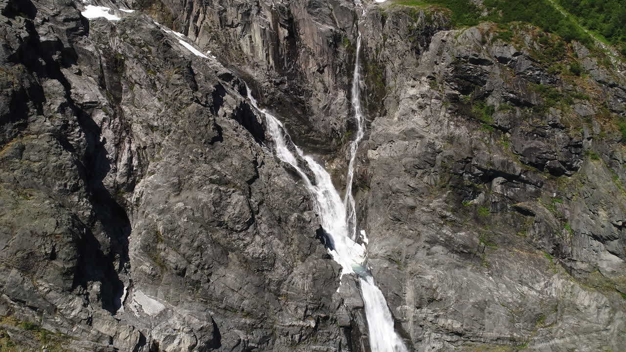un avión no tripulado se acerca a una dramática cascada que cae por escarpados acantilados rocosos en cámara lenta. filmado en la costa oeste de noruega.