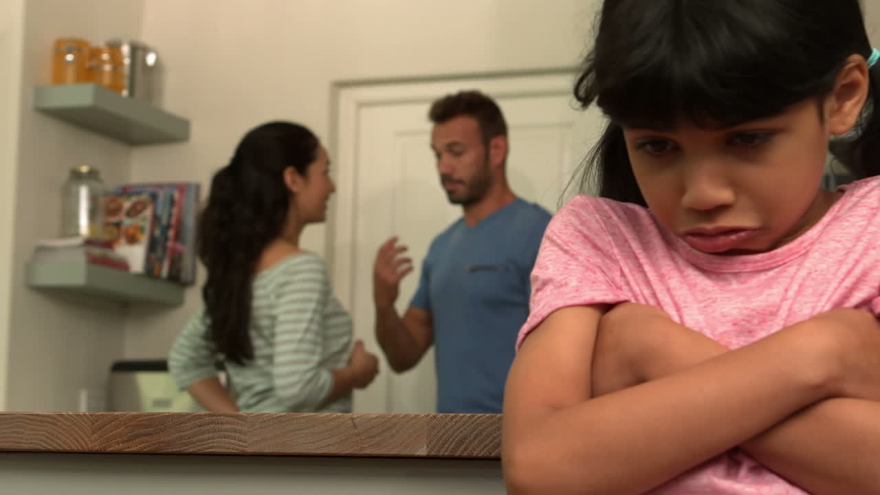 una niña triste escuchando a sus padres discutir.