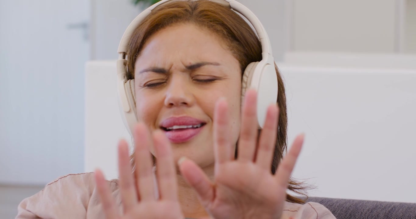 Donna afroamericana con top rosa e cuffie che ascolta musica, muovendo le labbra e le braccia sul divano