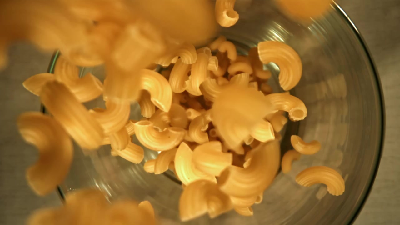 Maccheroni secchi che cadono in una ciotola di vetro al rallentatore