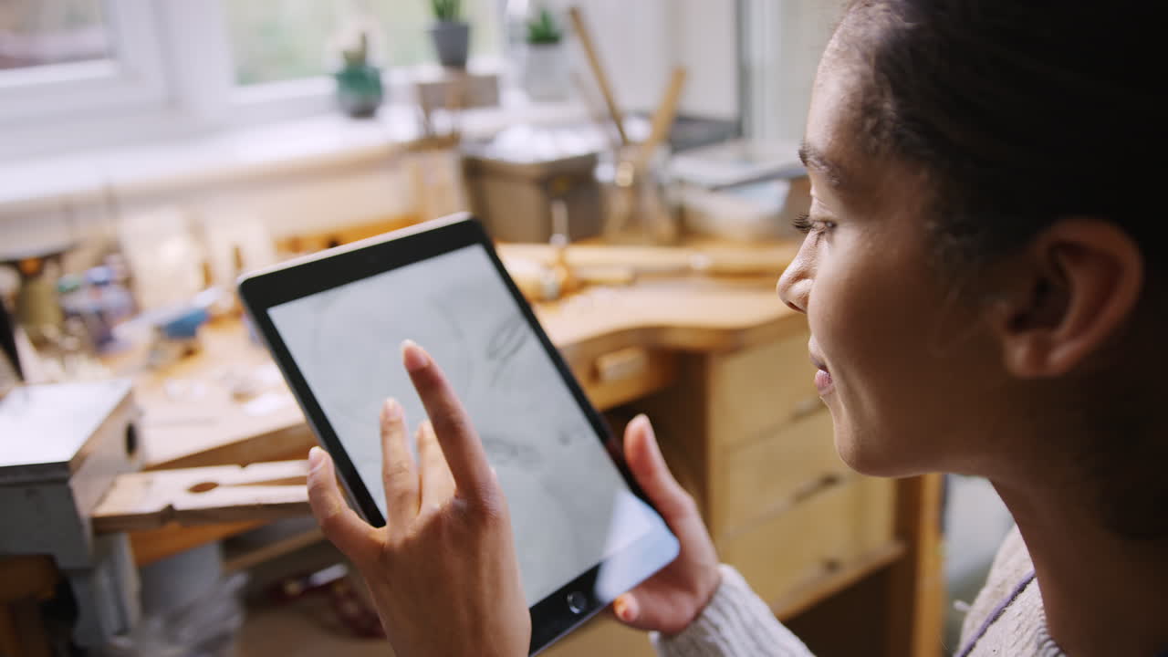 un primer plano de una joyera mirando el diseño de un anillo en una tableta digital en un estudio