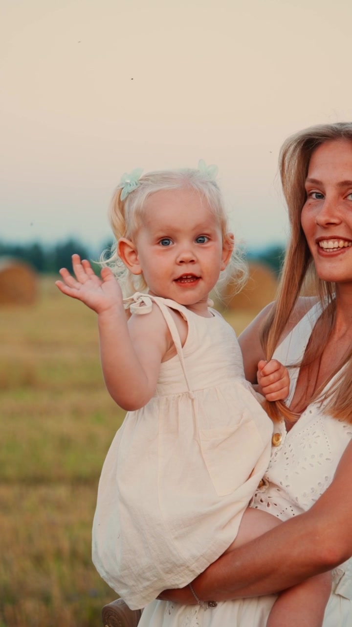 Junge Mutter hält ihre Kleinkindtochter bei Sonnenuntergang auf einem Feld