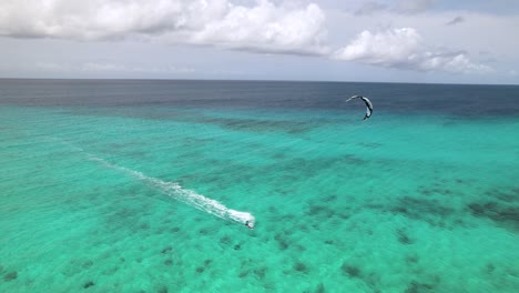 drone rastreando kite surfer cabalgando a través del agua del océano azul verde claro a la playa