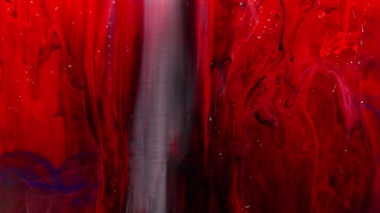 Vivid red ink swirling in dark water, fluid movement art closeup