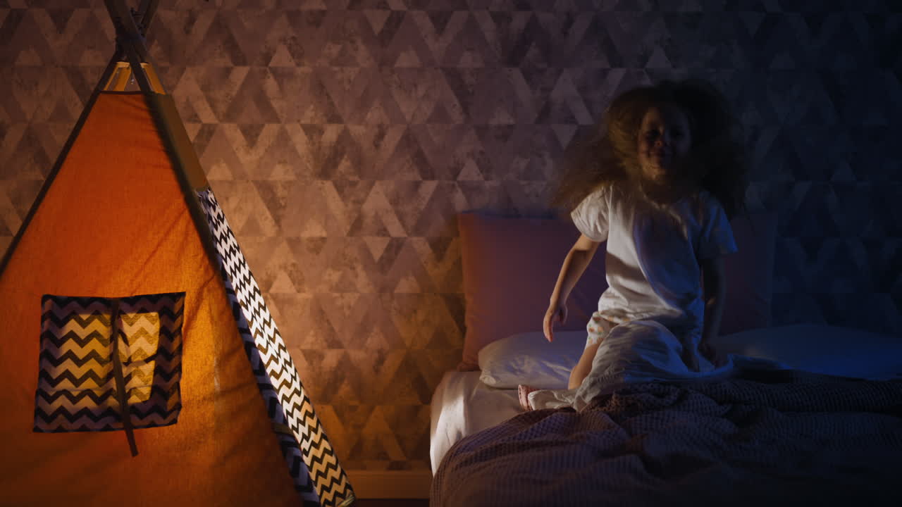 나쁜 작은 소녀는 침실에서 놀이 텐트 근처에 침대에 뛰어