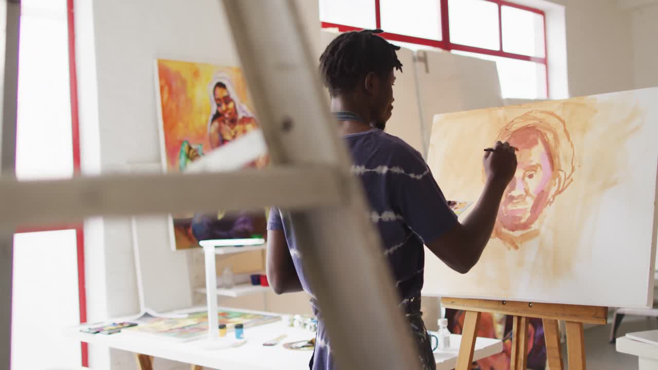 vista trasera de un artista masculino afroamericano con un delantal pintando en lienzo en un estudio de arte