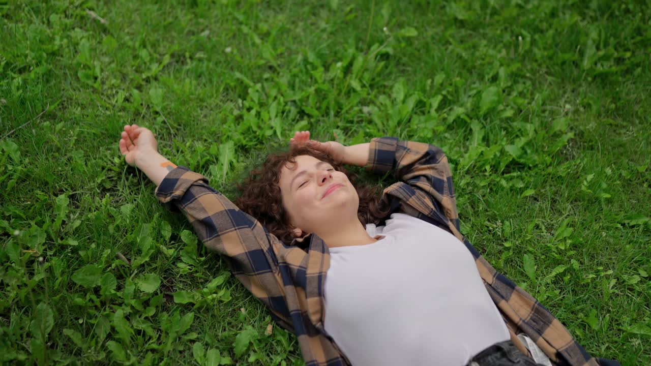 곱슬 머리카락을 가진 행복한 갈색 소녀는 공원의 녹색 잔디에 그녀의 등에 누워