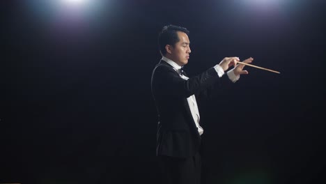 side view of asian conductor man holding a baton closing his eyes and showing gesture in the black studio