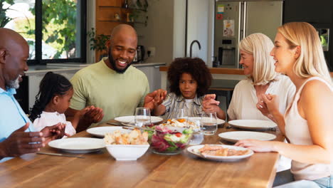 multi-generation family holding hands and saying prayer before meal at home