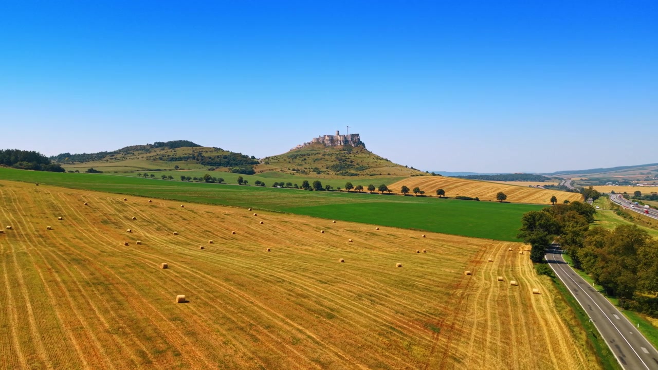 Campi di fieno e colline distanti. Campi agricoli sono coperti di balle di fieno e un'alta collina si erge sullo sfondo sotto un cielo azzurro e sereno.
